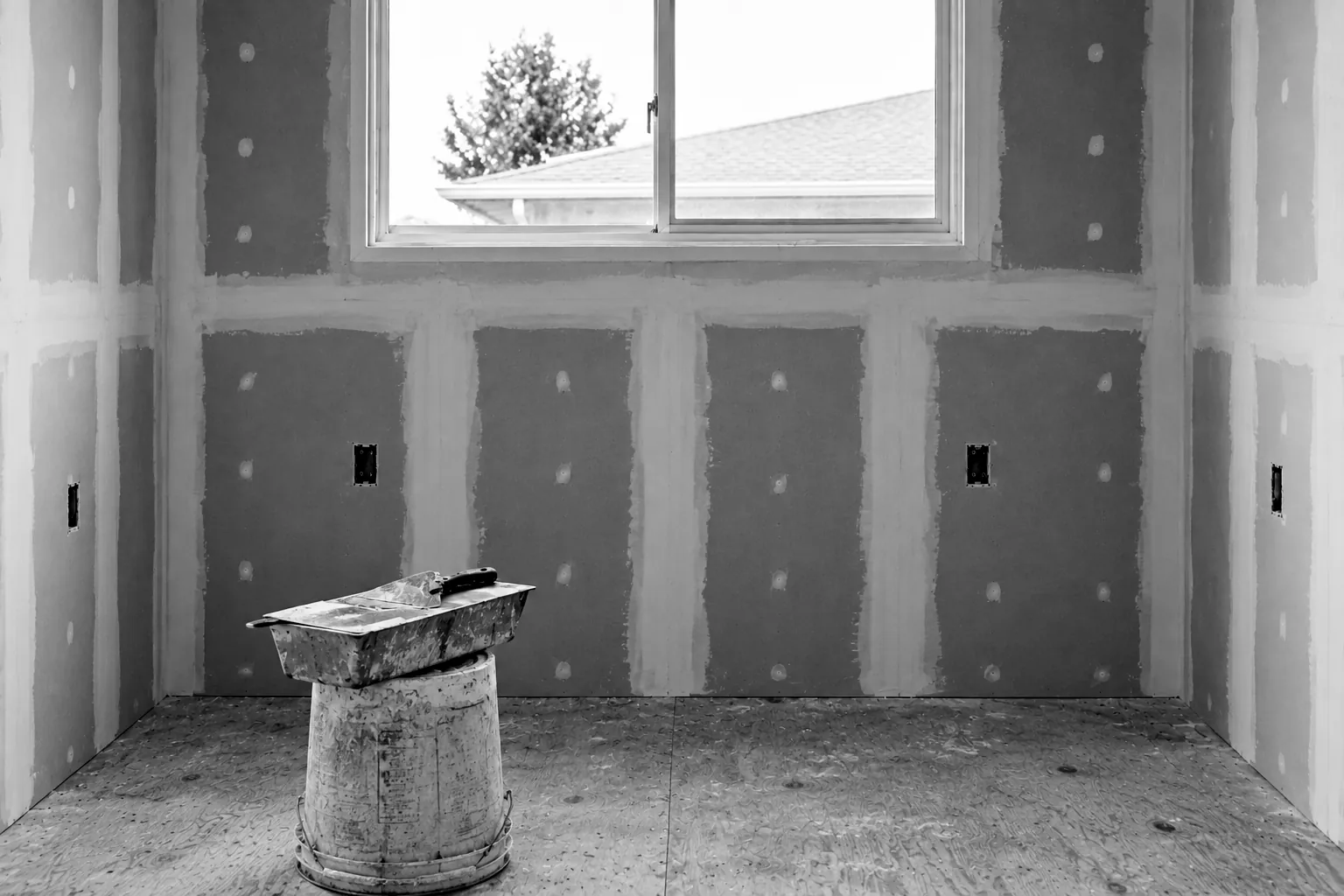 Render of new kitchen drywall with taped and mudded seams, and a mud pan resting on a bucket below the window.